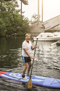 Portrait of smiling senior man paddleboarding in sea during sup course
