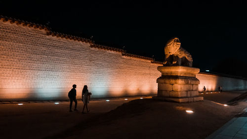 Silhouette people walking against illuminated historical building at night