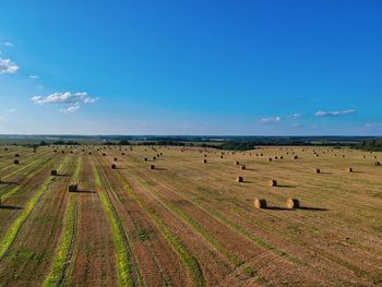 Hay bales on field against blue sky