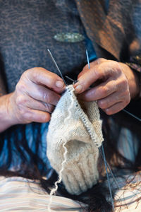 Unrecognizable elderly female using needles to knit warm apparel from natural yarn