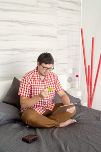 Young man using mobile phone while sitting on bed at home