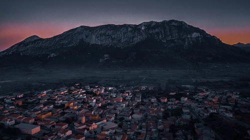 Aerial view of townscape by mountains against sky at sunset