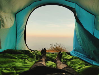 Low section of man relaxing in tent during sunset