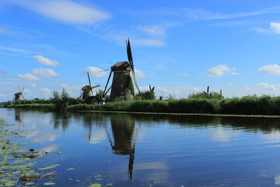 Traditional windmill by lake against sky