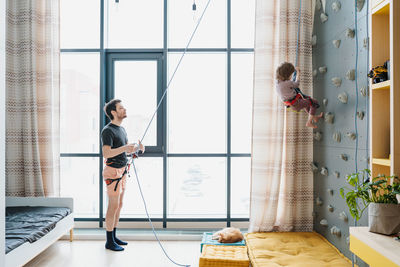 Young boy indoor rock climbing with his father instructor. hobby or home sport concept