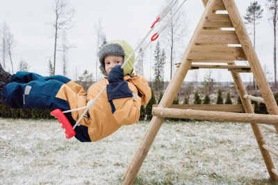 Close up of a boy swinging on a swing outside in winter