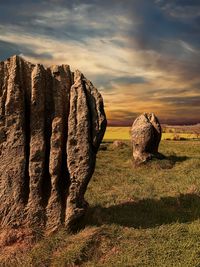 Rock formations on field against sky during sunset