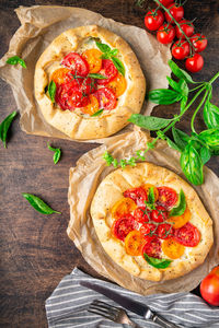 Fresh homemade galettes with tomatoes, ricotta cheese and basil on rustic plywood background.