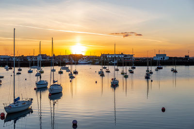 Boats moored in harbor at sunset