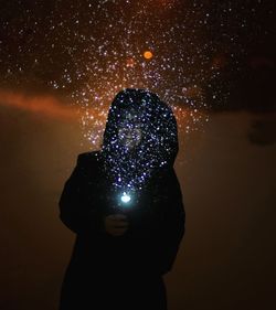 Close-up of silhouette hand holding camera against sky at night