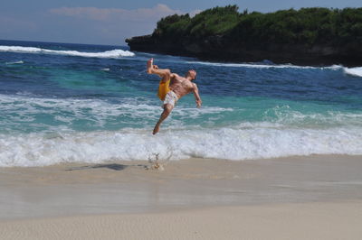 Man backflipping on beach against clear sky