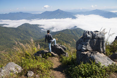 Man standing on the cliff and looking at the valley and mountains in the daylight