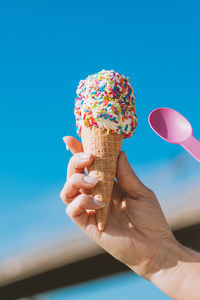 Cropped hand of woman holding ice cream against sky