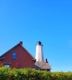 Low angle view of lighthouse against buildings against clear blue sky