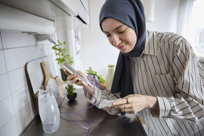 Woman in headscarf unpacking groceries at home and checking receipt