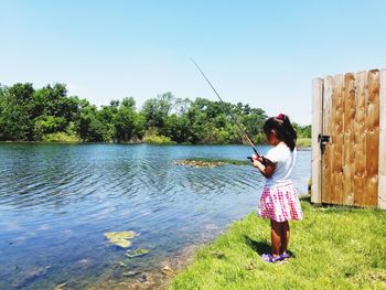 Full length of woman fishing in lake against clear sky