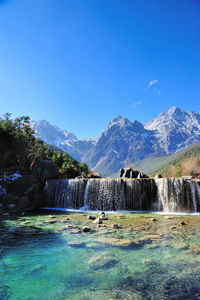 Scenic view of waterfall against blue sky