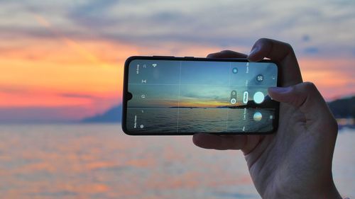 Man photographing with smart phone against sunset sky