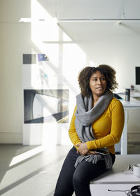 Businesswoman with mobile phone looking away while sitting on desk in office