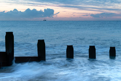 Wooden posts in sea against sky during sunset