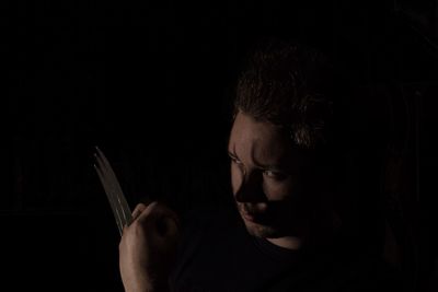 Close-up of man wearing weapon in hand against black background