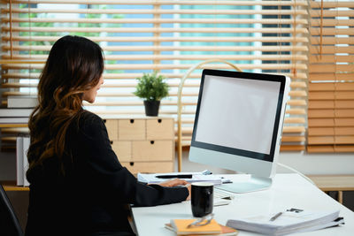 Rear view of woman using laptop at office