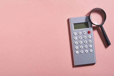 High angle view of calculator and mobile phone on pink background