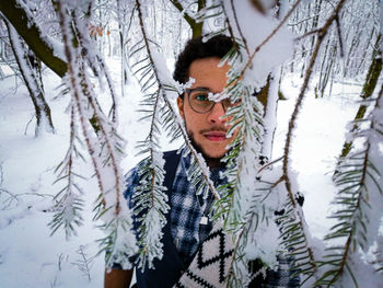 Portrait of man with snow on tree trunk during winter