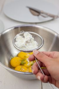 Cropped hand holding strainer with flour over egg yolk in bowl