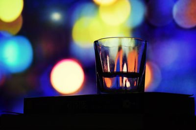 Close-up of drinking glass against illuminated defocused lights