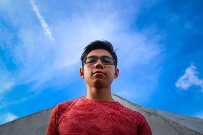 Low angle portrait of young man standing against sky