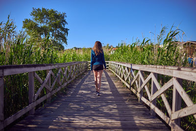 Rear view of woman on footbridge against sky