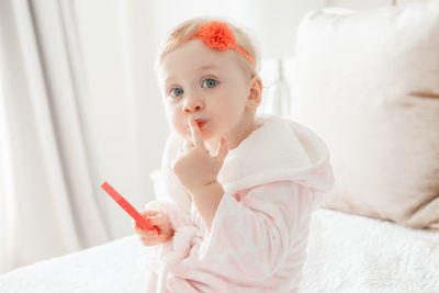 Portrait of cute girl applying make-up while sitting on bed at home