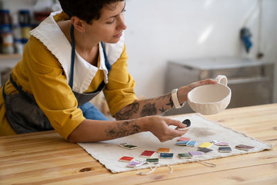 Craft crockery making. woman artist choose paint color for handmade cup in studio for online orders