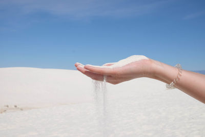 Cropped hand of woman holding sand at beach against blue sky during summer