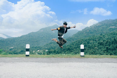 Rear view of man jumping on road against sky