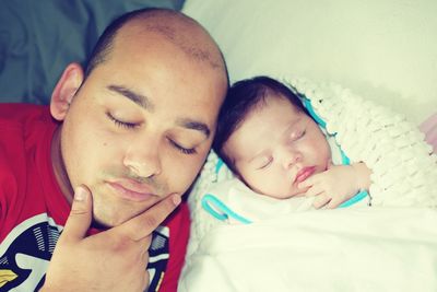 Close-up of man with eyes closed by sleeping daughter