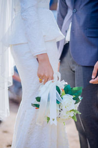 Midsection of bride holding bouquet while standing with groom during wedding ceremony