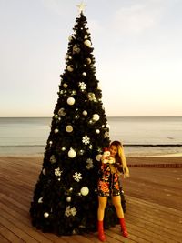 Woman standing by christmas tree on promenade against sea