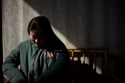 Woman wearing jacket while sitting against curtain at home