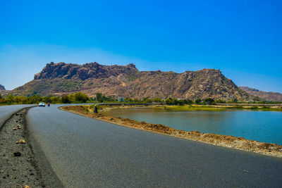 Road by mountains against clear blue sky