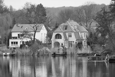 Houses and trees by lake against buildings