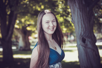 Portrait of smiling young woman standing against trees