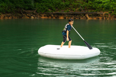 Young boy wearing life jackets paddling on an inflatable boat in kenyir lake, malaysia.