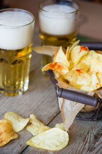 High angle view of fresh potato chips in metal basket by beers on table