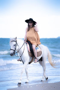 Young woman riding horse on sea shore against sky