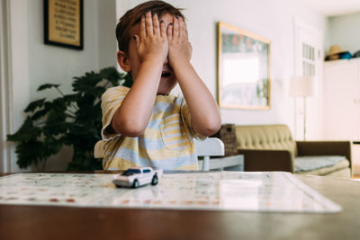 Toddler sitting at table playing peekaboo and covering his eyes