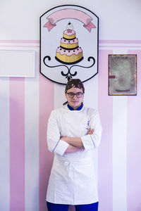 Portrait of confident male baker with arms crossed standing against wall in laboratory