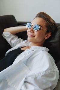 Portrait of young woman wearing sunglasses while sitting against white background