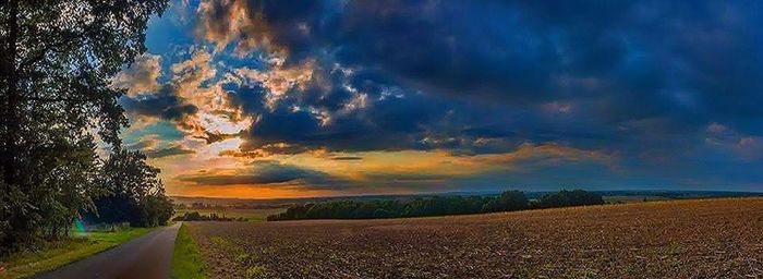 Road amidst field against sky during sunset